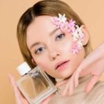 Woman with flower-adorned face holding a perfume bottle.