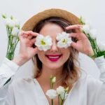 Woman holding flowers to her eyes, smiling with a straw hat