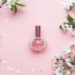 Perfume bottle surrounded by white flowers on pink background